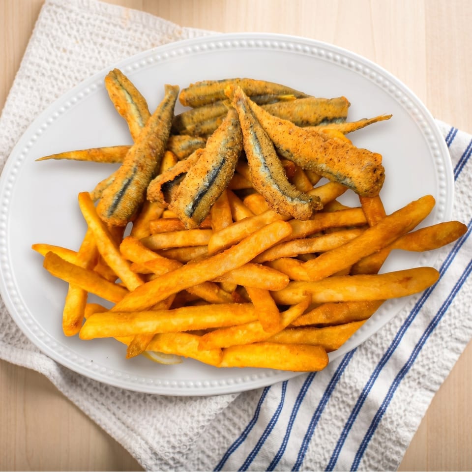 A white plate holds crispy fried fish and golden french fries on a white and blue striped napkin.